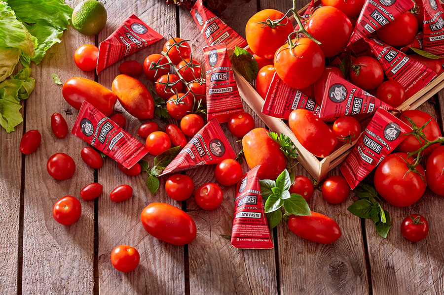 One-use paper-packaged KYKNOS tomato paste among tomatoes.